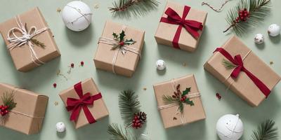 The primary subject of the image is a collection of six Christmas presents, each wrapped in brown paper and tied with a bow. The presents are placed on a green surface, which serves as the setting for the scene. The visual style of the image is a photo, capturing the details of the presents and their surroundings. The colors and mood of the image are warm and festive, as the presents are associated with the holiday season.